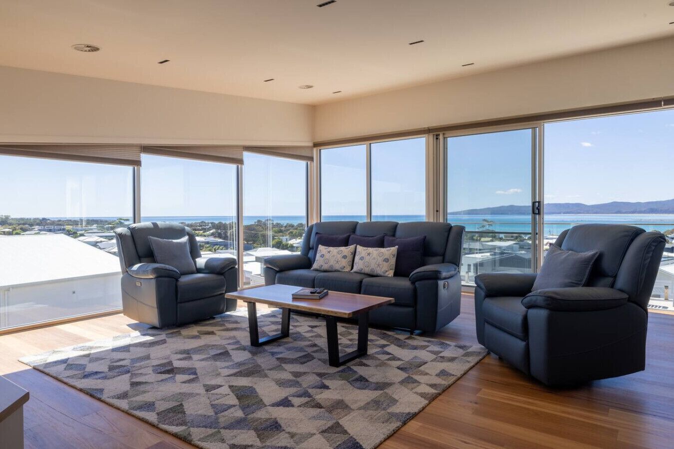 Un salon moderne comprenant un canapé, deux fauteuils, une table basse et de grandes fenêtres donnant sur la mer.