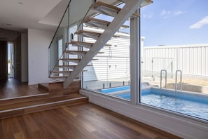Ein modernes Interieur mit einer Holztreppe, einem großen Fenster mit Blick auf einen Pool und einer Ansicht eines weißen Gebäudes.