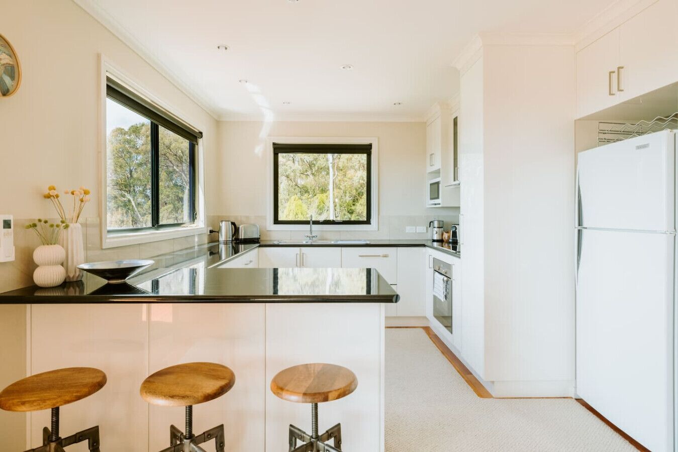 A modern kitchen with a central island, white cabinetry, and bar stools.