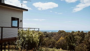 A modern building with a metal exterior, a small window, and a balcony overlooking a forested landscape with a distant view of the sea. - Panorama Escape, Port Sorell (Port Sorell)
