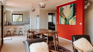 A modern dining area with a wooden table and chairs, a red accent wall, and a large abstract painting. - Panorama Escape, Port Sorell (Port Sorell)