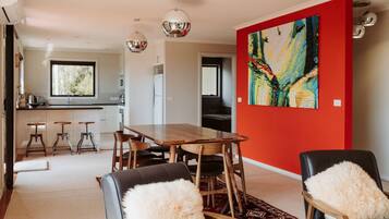 A modern dining area with a wooden table and chairs, a red accent wall, and a large abstract painting.