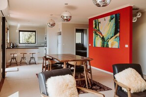 Et moderne spiseområde med et træbord og stole, en rød farveaccent på væggen og et stort abstrakt maleri.