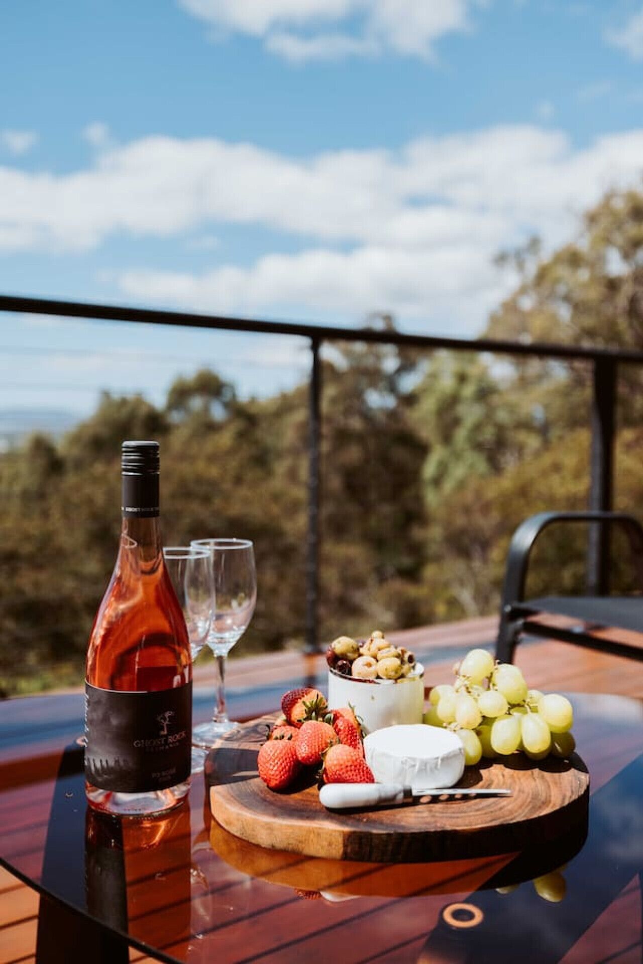 Une table avec une bouteille de vin, des verres, des fraises, du fromage et des raisins, le tout disposé sur une planche en bois.