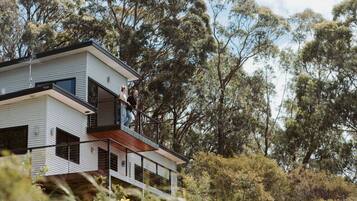 A modern two-story house with a balcony, surrounded by trees.