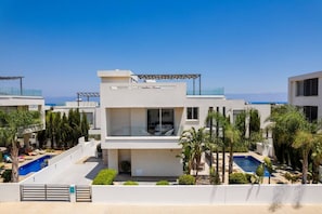 Ein modernes, mehrgeschossiges Gebäude mit Pool, umgeben von Palmen und freiem Blick auf das Meer.