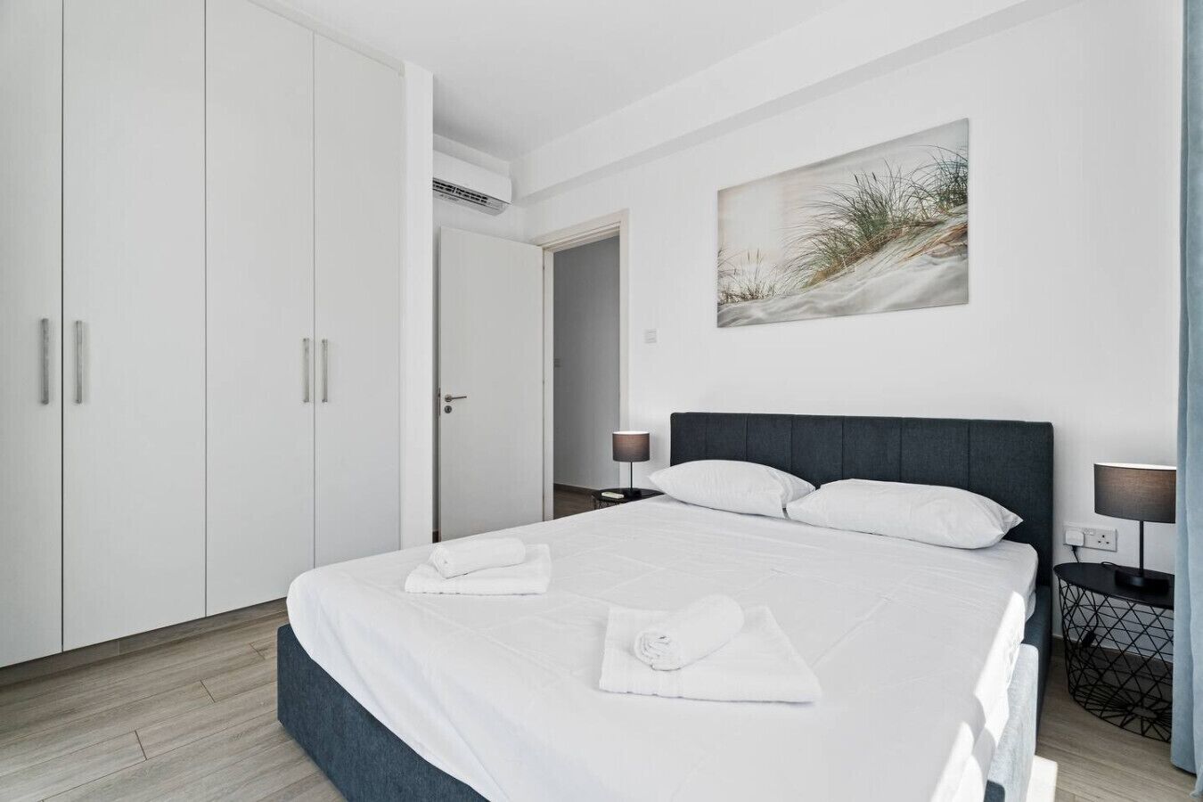 Une chambre à coucher avec un lit, une armoire blanche, des œuvres d’art, des lampes de chevet et une table de chevet.