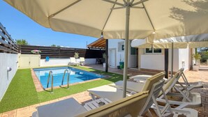Ein Pool mit Sonnenschirm, Liegestühlen und einer kleinen Gartenanlage.