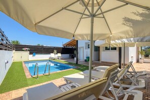 A swimming pool with a sunshade, lounge chairs, and a small garden area.