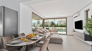 Un salon moderne comprenant un coin repas, un téléviseur et donnant sur une piscine.