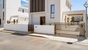 Un bâtiment moderne à deux étages, doté d’une façade blanche, d’une grande fenêtre verticale et d’une entrée fermée par un portail.
