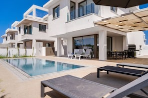 Eine moderne Villa mit Swimmingpool, Sitzgelegenheit im Freien und Grillplatz.