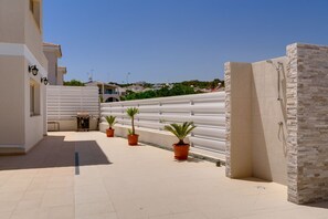A covered outdoor area with a white fence, potted plants, and a stone wall. - Anthorina Gardens Retreat (Paralimni)