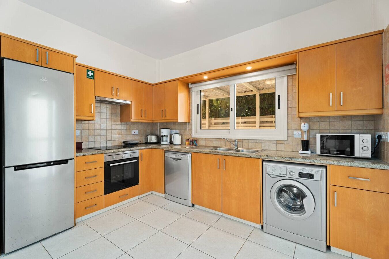 A modern kitchen with stainless steel appliances, wooden cabinets, and a large window.