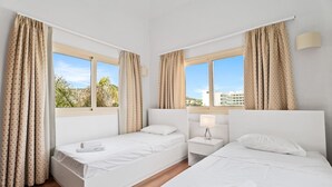 Ein Hotelzimmer mit zwei Betten, einem Nachttisch und einem Fenster mit Vorhängen.