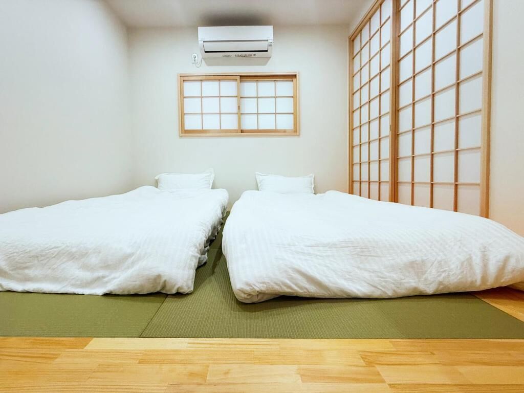 A room with two beds, a window with a grid pattern, and an air conditioning unit.