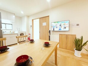 A dining area with a wooden table, chairs, a television mounted on the wall, and a potted plant. - shio (Osaka)