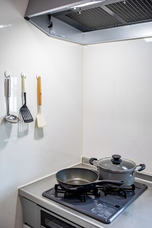 A kitchen with a stove, a frying pan, and a pot on it. There are two spatulas hanging on the wall. - shio (Osaka)