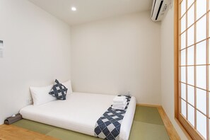 Ein Einzelbett mit einer gemusterten Decke, einem Kopfkissen und einem gefalteten Handtuch auf einer Futonliege.