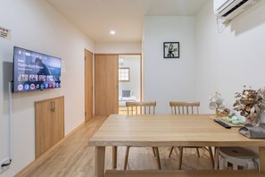 A modern dining area with a wooden table, chairs, and a television displaying a streaming service. - shio (Osaka)