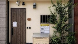 Un edificio a due piani con una porta in legno, un piccolo spazio esterno con posti a sedere e un cartello con scritte.