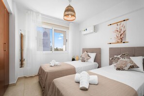 Ein Hotelzimmer mit zwei Betten, einem Fenster mit Aussicht, einer Hängelampe und einer Klimaanlage.