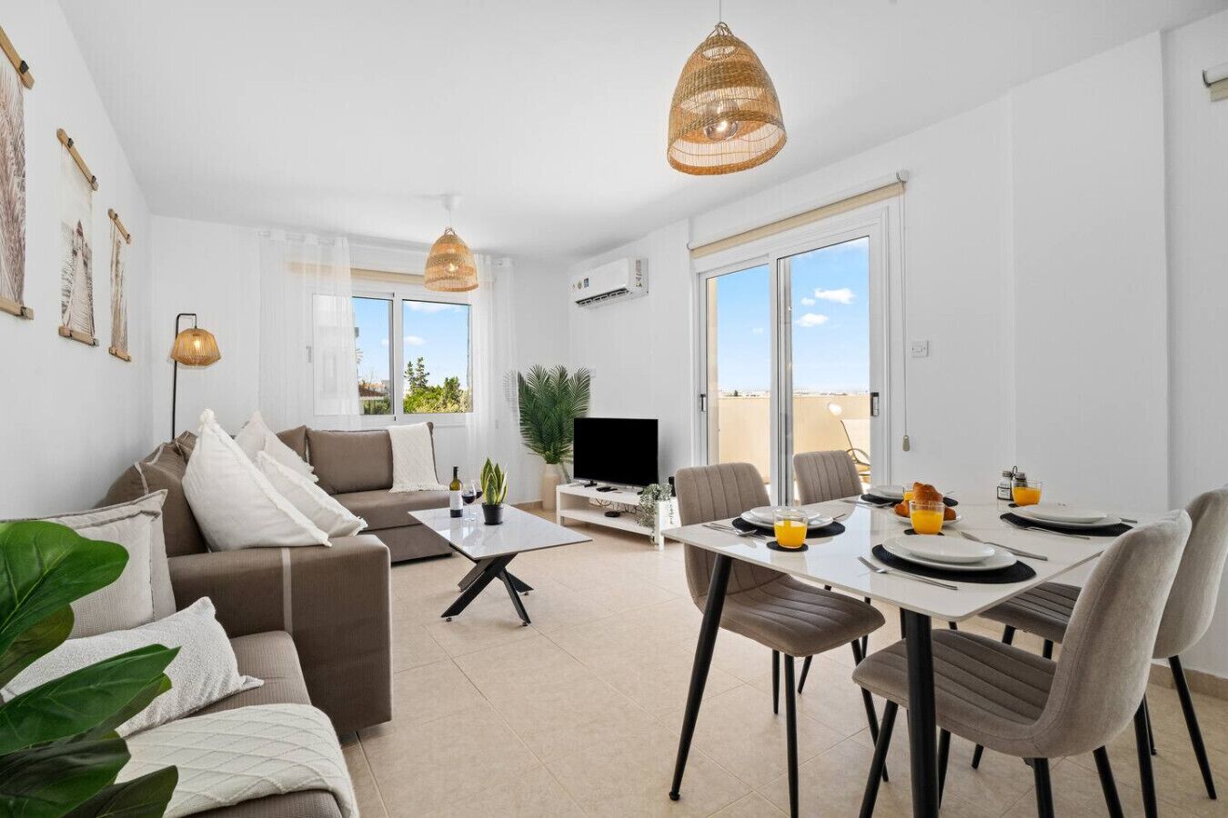 Un salon moderne comprenant un canapé, une table basse, une table à manger et des chaises. On y trouve également un téléviseur, une plante et une fenêtre donnant sur un beau paysage.