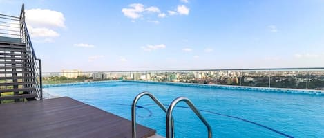 A rooftop pool with a city view, metal pool ladders, and a wooden deck.
