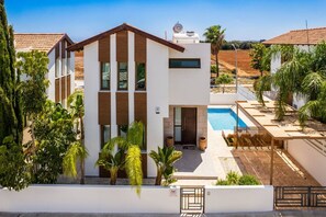 A modern two-story house with a swimming pool, surrounded by greenery and a clear sky.