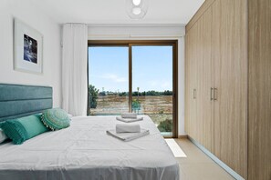 A bedroom with a large bed, a view of a field, and a wooden wardrobe.