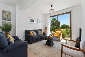 A modern living room with a sofa set, a coffee table, and a chair. There are framed pictures on the wall and a plant on the left.