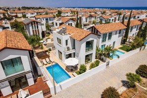 A modern residential area with white buildings, red-tiled roofs, and a swimming pool.