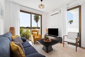 A modern living room with a sofa, armchairs, a coffee table, a TV, and large windows with a view.