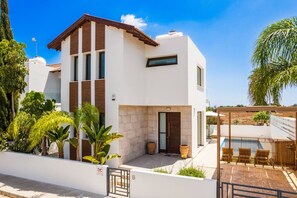 A modern two-story house with a patio, a pool, and a view of the surrounding landscape.