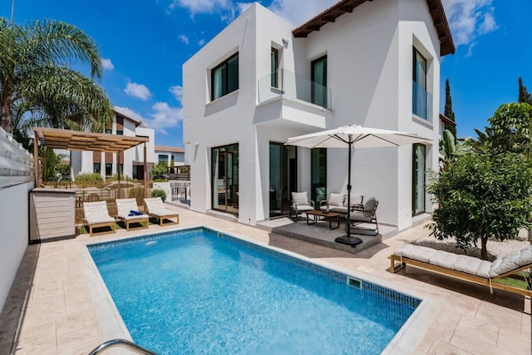 A modern two-story house with a swimming pool, outdoor seating, and a pergola.