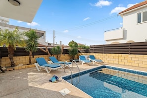 Ein Schwimmbecken mit Liegestühlen, einer gefliesten Terrasse und einer Backsteinmauer.