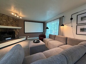 Ein Wohnzimmer mit Kamin aus Stein, einem großen Flachbildfernseher, einer Couch und einem Fenster mit Vorhängen.