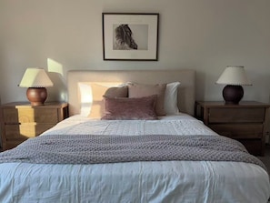 Ein Schlafzimmer mit einem Bett, zwei Nachttischen, einem gerahmten Bild an der Wand und zwei Lampen.