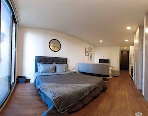 Ein modernes Schlafzimmer mit einem großen Bett, einem runden Spiegel, einem Flachbildfernseher und einem begehbaren Kleiderschrank.