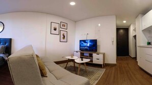 Ein modernes Wohnzimmer mit Sofa, Fernseher, kleinem Tisch und Küchenzeile.