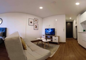 A modern living room with a sofa, TV, small table, and a kitchen area. - Modern Studio Apartment (Bogotá)