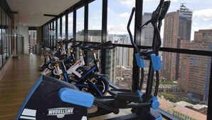 Ein Fitnessraum mit Ergometer und Laufbändern, große Fenster mit Blick auf die Stadt.