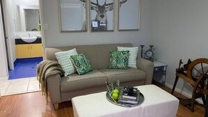 A living room with a sofa, a coffee table with books and apples, a clock, and framed deer antlers on the wall. - Room-relax & Unwind on the Gold Coast (Gold Coast)