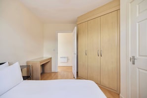 Ein Schlafzimmer mit einem Bett, einem Holztisch, einem Kleiderschrank und einer Tür zu einem anderen Raum.