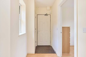Ein schmaler Flur mit einer weißen Tür am Ende, einem kleinen Fenster zur linken und einer Holztür zur rechten.