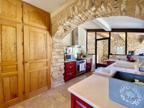 A kitchen with wooden cabinets, a stone wall, and a view of the outdoors. - Large farmhouse in Bonnieux, with a fenced-in pool and air conditioning (Bonnieux)