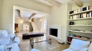 Un salón amplio con un sofá blanco, una mesa de centro de vidrio, una chimenea y una estantería llena de libros.