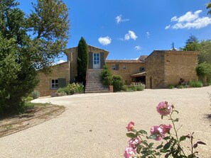 A stone building with a central staircase, a door, and a garden with pink flowers.