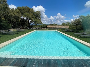 A rectangular swimming pool with clear blue water, surrounded by a grassy area with lounge chairs and trees.