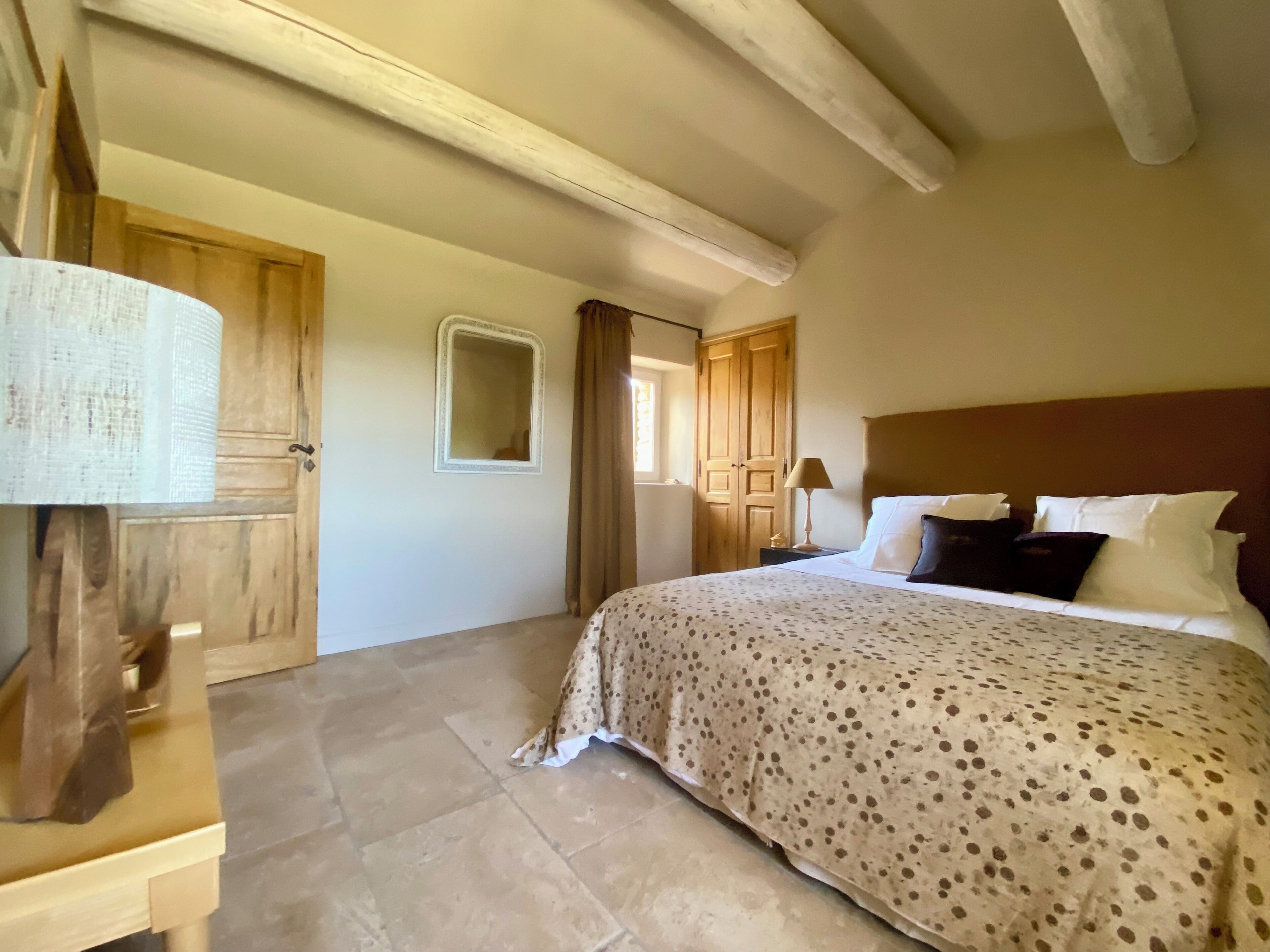 Un dormitorio con cama, armario de madera, un espejo y ventana con cortinas.